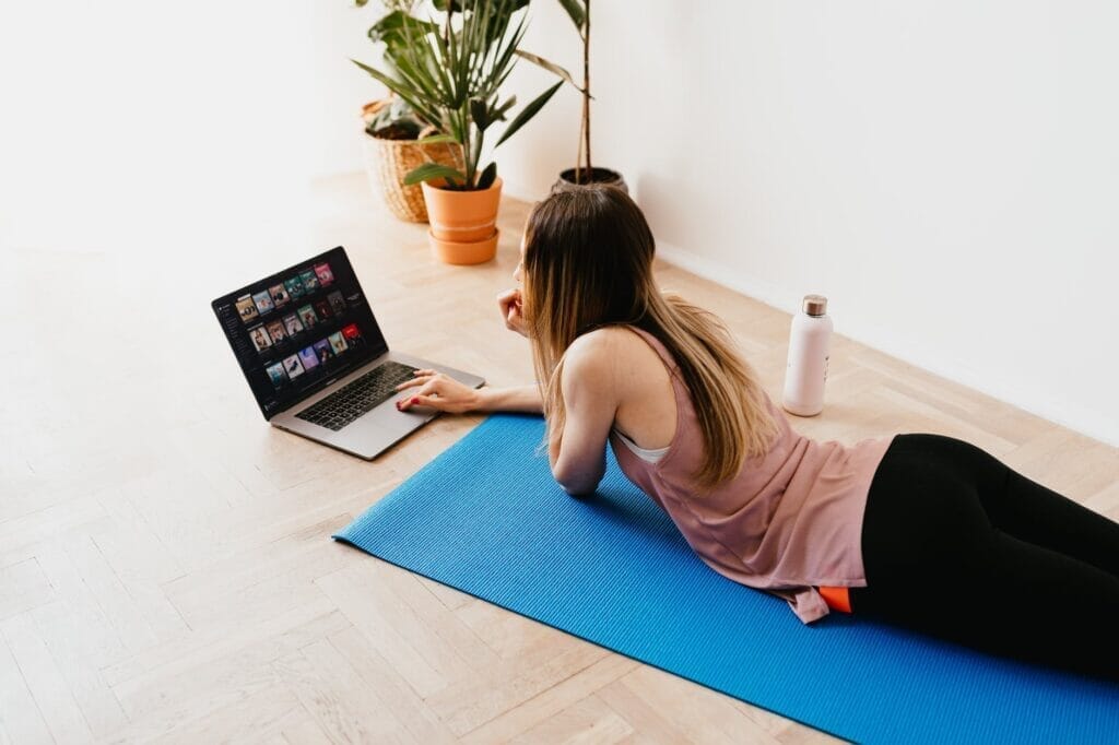 young woman lying on floor on mat while using laptop at home