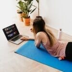 young woman lying on floor on mat while using laptop at home