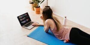 young woman lying on floor on mat while using laptop at home